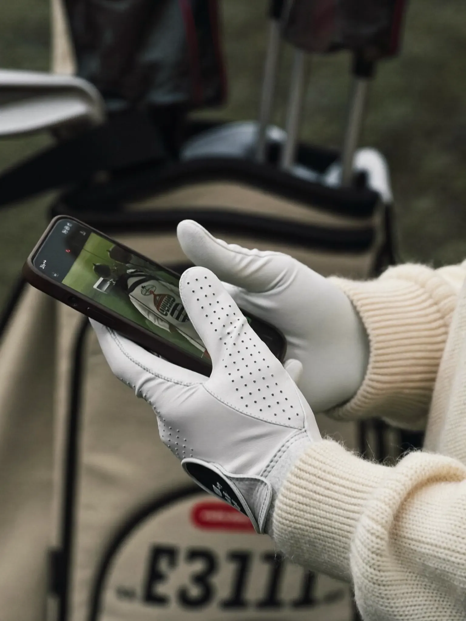 Gloved hands holding a phone beside a golf bag