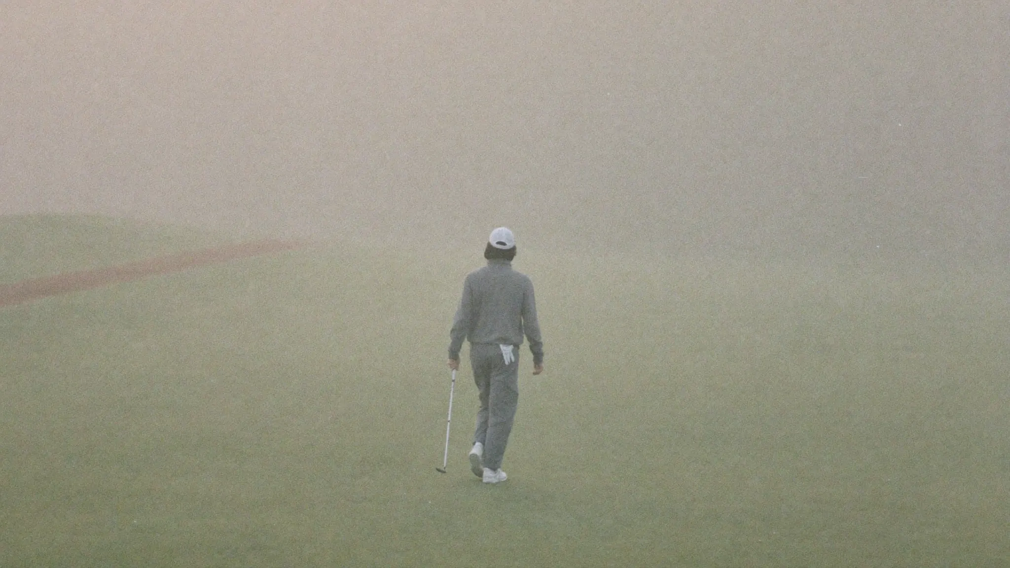 A golfer walking alone down a misty fairway